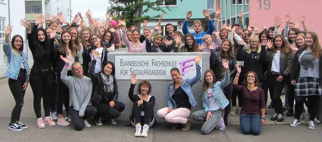 Strahlende Schülerinnen präsentieren sich am Eingangsschild der Evangelischen Fachschule für Sozialpädagogik Reutlingen.