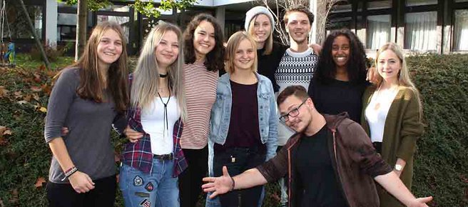 In der Sonne sitzt eine Gruppe von Schülerinnen vor dem Eingang der Evangelischen Fachschule für Sozialpädagogik Schwäbisch Hall.